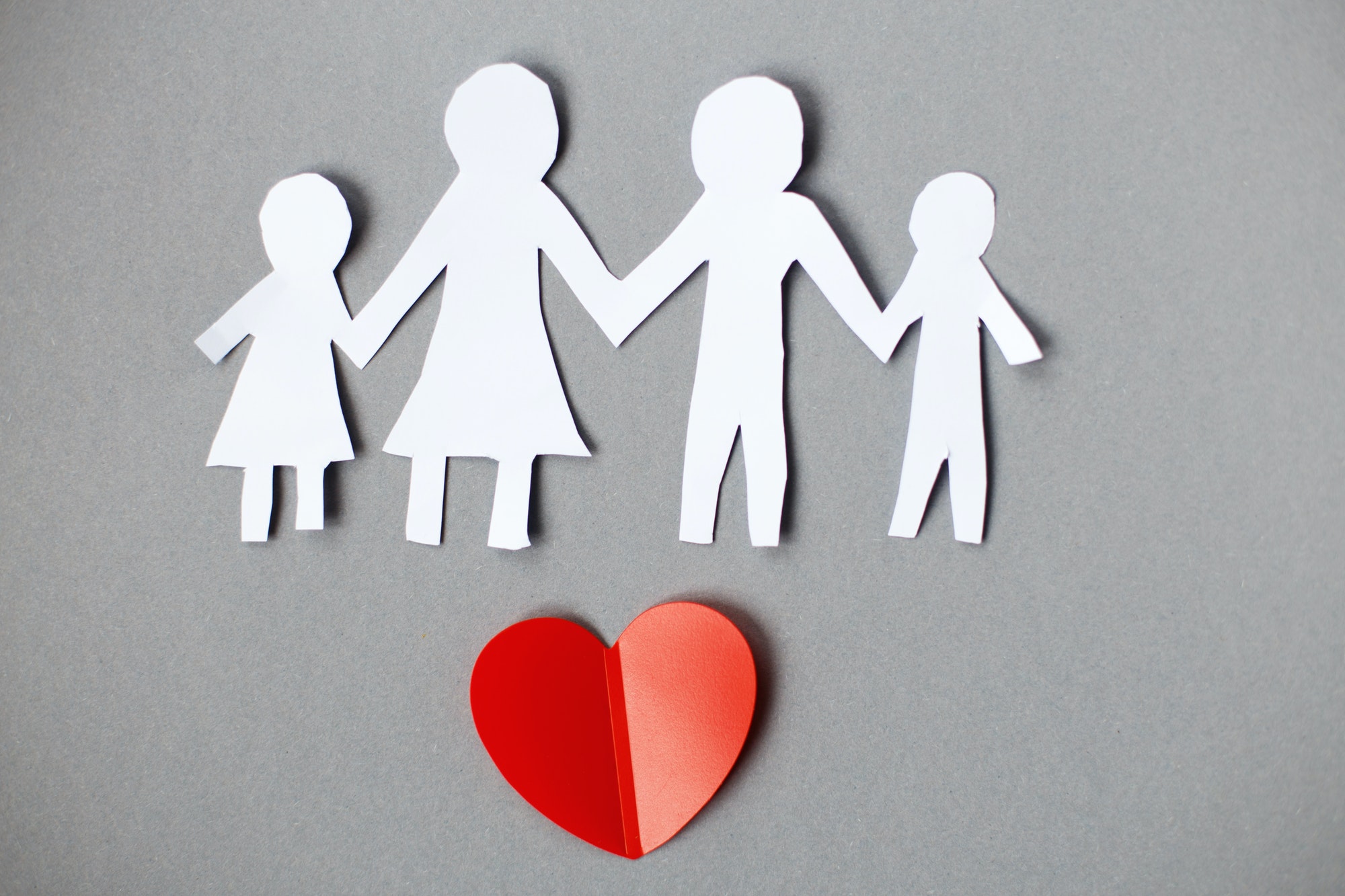 Happy paper cut family holding hands on gray background with red heart
